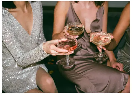 Two women in party dresses raising coupe style champagne glasses with a third woman out of shot