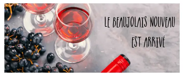 Glass of light coloured red Beaujolais wine with black grapes and caption "Le Beaujolais nouveau est arrivé!"