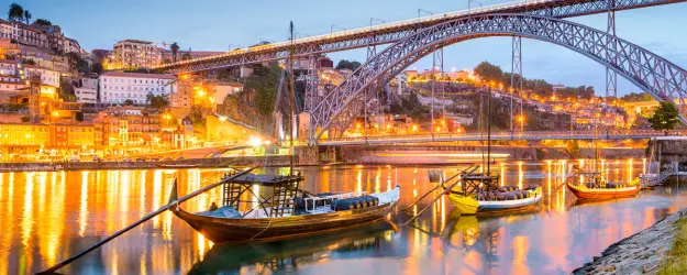 An evening view of Porto harbour with metal bridge over the river Douro and some traditional boats