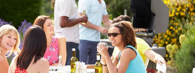 Group of riends stiing in the sun at a table with wine and barbecue food