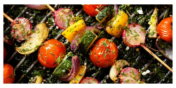 Skewers of cherry tomatoes, courgettes and red onion cooking on a barbecue