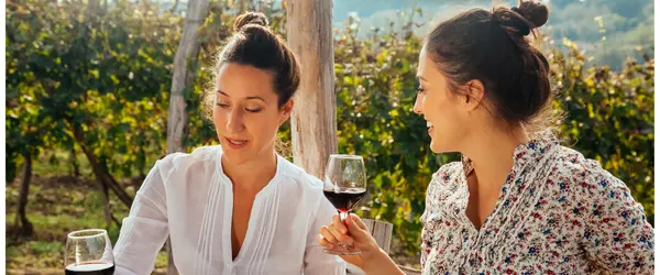 Two women sitting outside in the sun each enjoying a glass of red wine