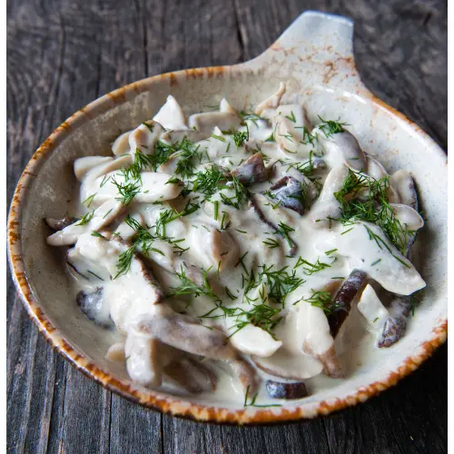 A dish containing some mushrooms cooked in a creamy sauce and with some green herbs on top