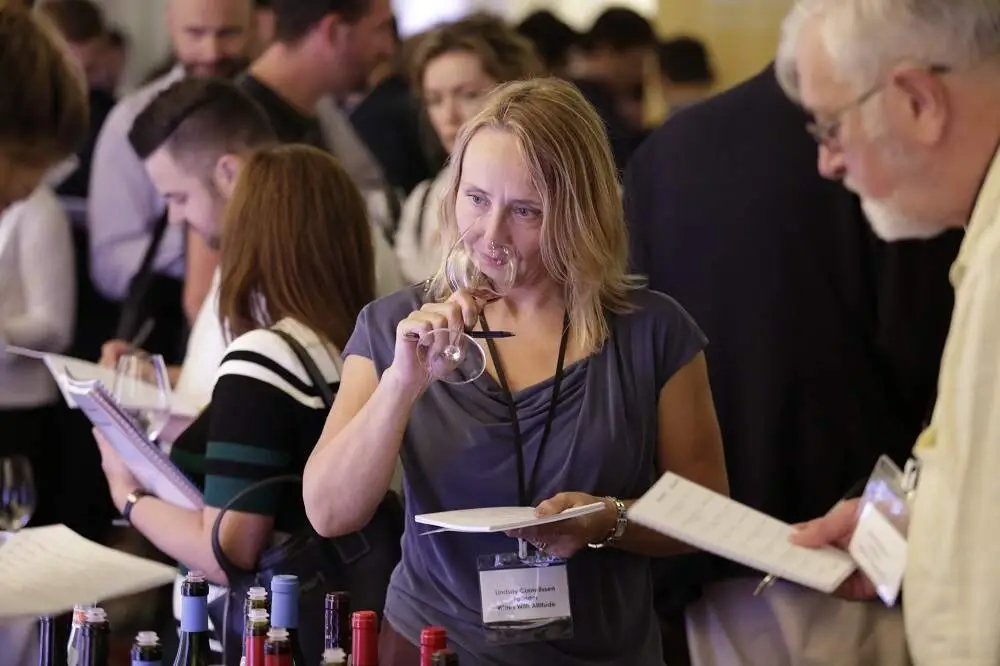 Lindsay Cornelissen founder of Wines With Attitude smelling wine at a tasting surrounded by people writing notes and tasting wine