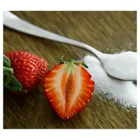 Strawberries next to a teaspoonful of sugar on a wooden table