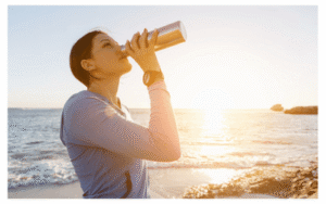 Woman on the sea shore in the sun drinking from a water bottle
