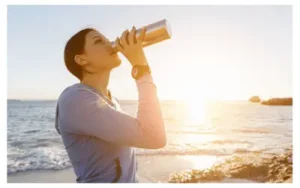 Woman on the sea shore in the sun drinking from a water bottle
