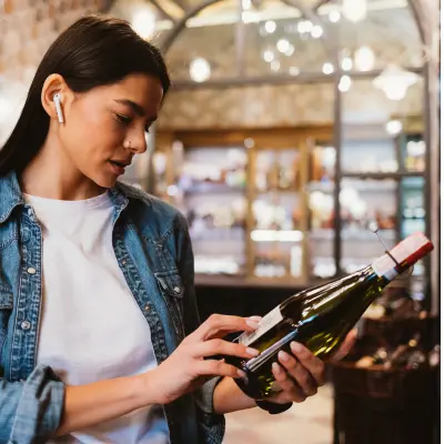 A young woman wearing white t-shirt and denim jacket reading the back label of a bottle of white wine