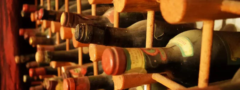 Several wine bottles in wine rack, some with old labels and broken foils suggesting they are old wines