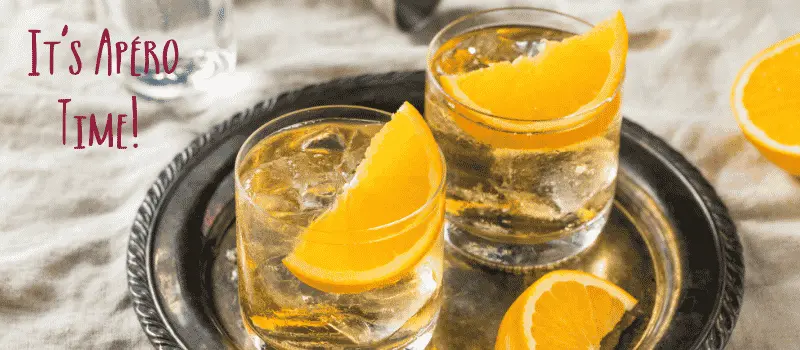 Two glasses of a white wine cocktail with a slice of orange in each on a silver platter
