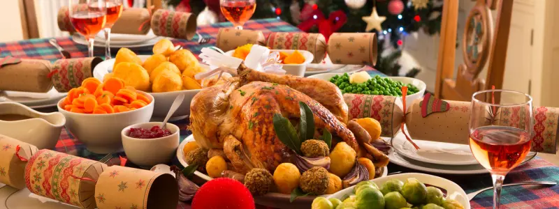 A typical Christmas dinner table with a turkey, bowls of vegetables, crackers and glasses of wine