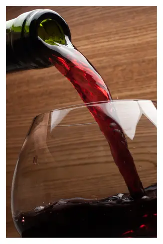 Red wine being poured from the tip of a bottle into a large glass