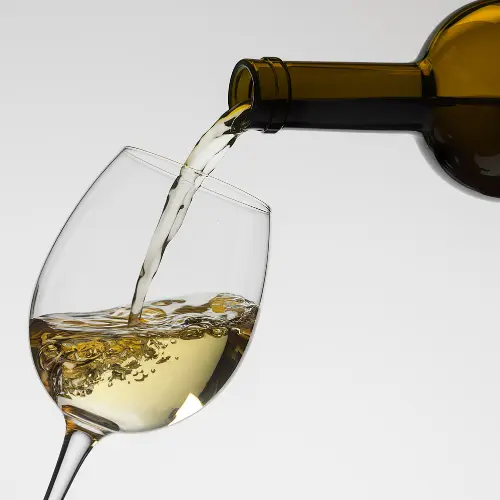 Glass of white wine being poured from a bottle