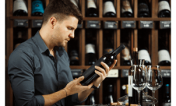 A man infromnt of some wooden wine shelves studying a wine label