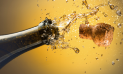 Top of a bottle of sparkling wine with the cork exploding out against a yellow background