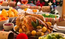A typical Christmas dinner table with a turkey, bowls of vegetables, crackers and glasses of wine