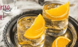 Two glasses of a white wine cocktail with a slice of orange in each on a silver platter